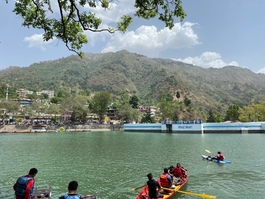 Colorful boats resting on the serene waters of Naukuchiatal Lake surrounded by lush green hills, located just minutes from Ethnic Trail Wooden Heritage Homestay