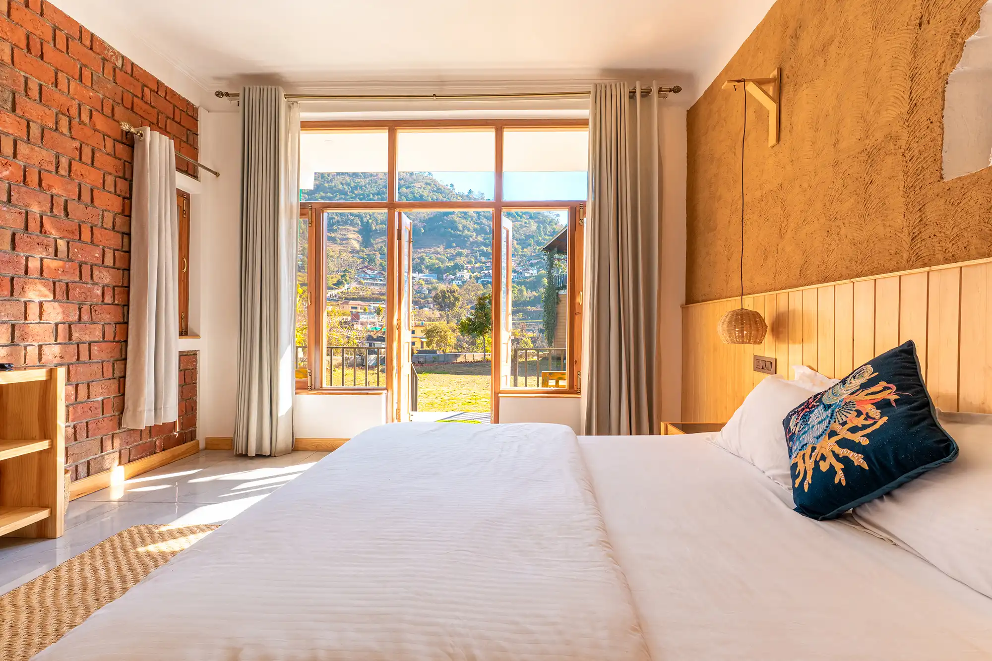 "Cozy wooden bedroom featuring a large window framing a lush green mountain view at Ethnic Trail heritage homestay in Thapaliya Mehragaon, Naukuchiatal."